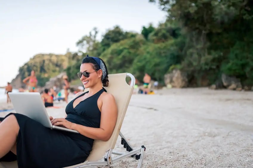 Smiling woman sitting at the beach with laptop