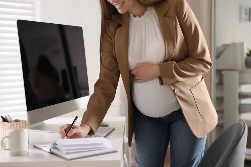 Standing, a pregnant woman writing in notebook